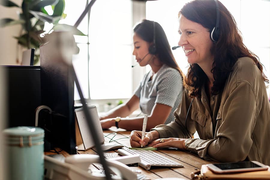 Customer service representatives engaged in training workshop, discussing donor issues and solutions, with headsets and computers in a collaborative workspace.