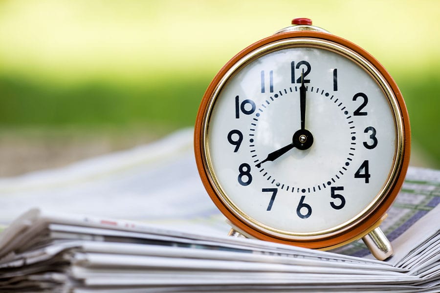 Clock displaying time with emphasis on time management and delegation, positioned on a stack of newspapers, symbolizing productivity and efficiency in a professional training context.
