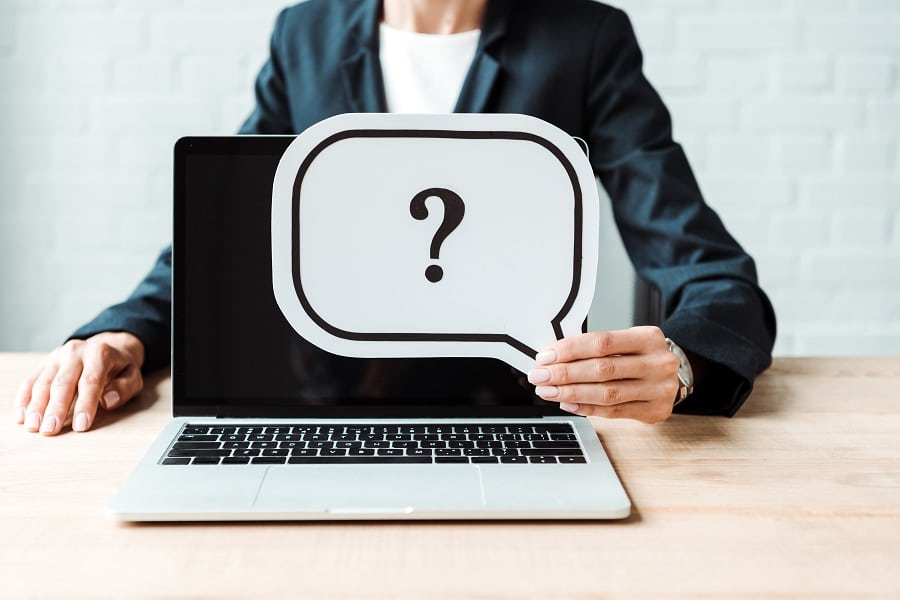 Woman in business attire holding a speech bubble with a question mark in front of a laptop, symbolizing inquiry and engagement in sales conversations.