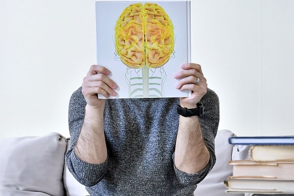 Person holding a book with a brain illustration, symbolizing knowledge and emotional intelligence in a learning environment.