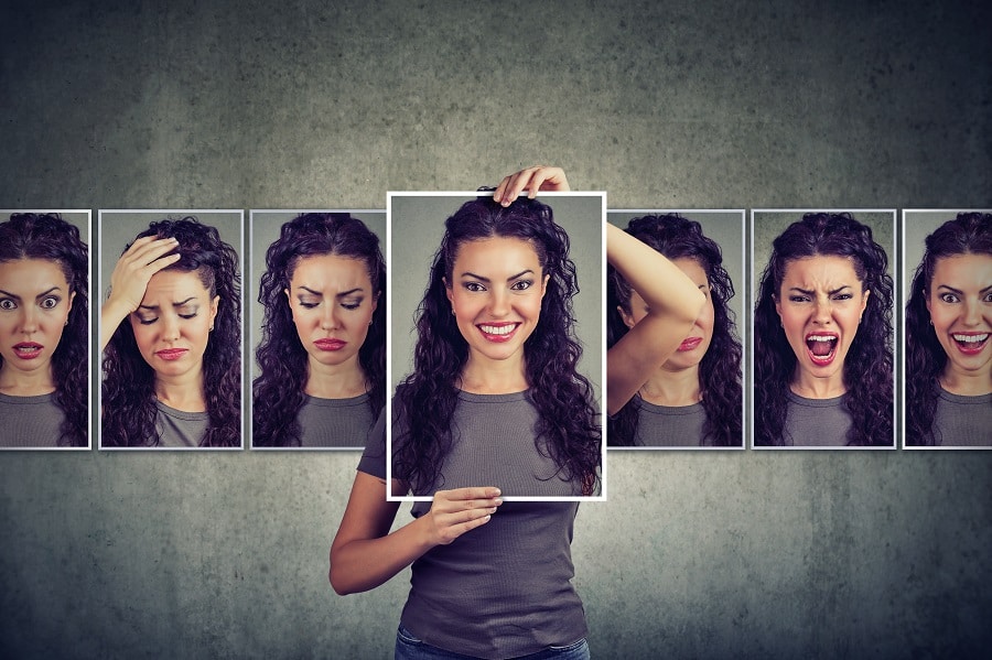 Woman displaying a range of emotions, holding a photo frame with a smiling face, surrounded by images of various emotional expressions, illustrating emotional intelligence and adaptability.