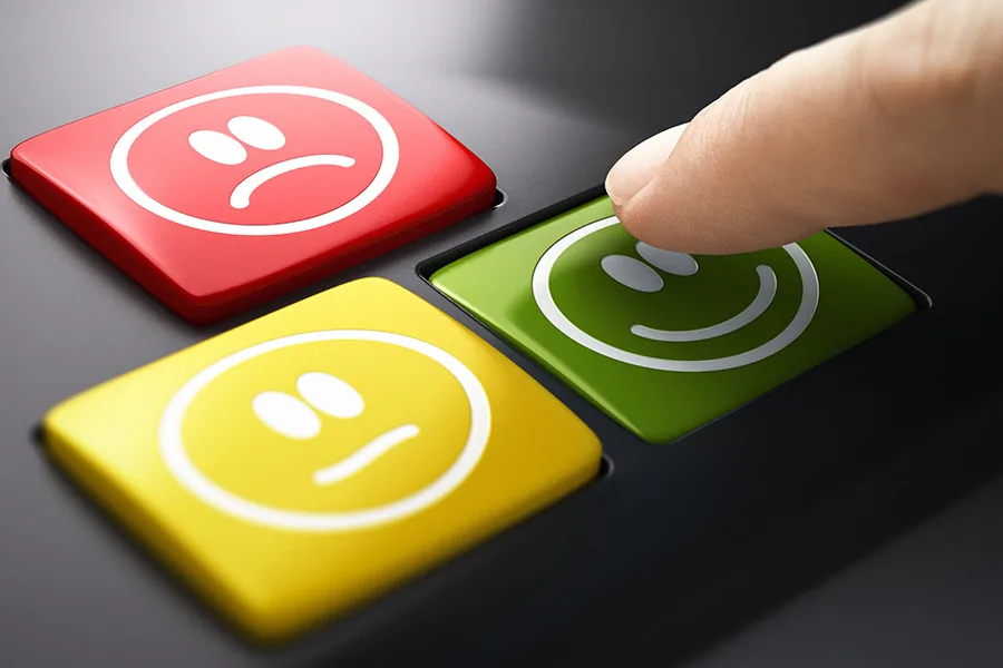 Finger pressing a happy face button beside neutral and unhappy face buttons