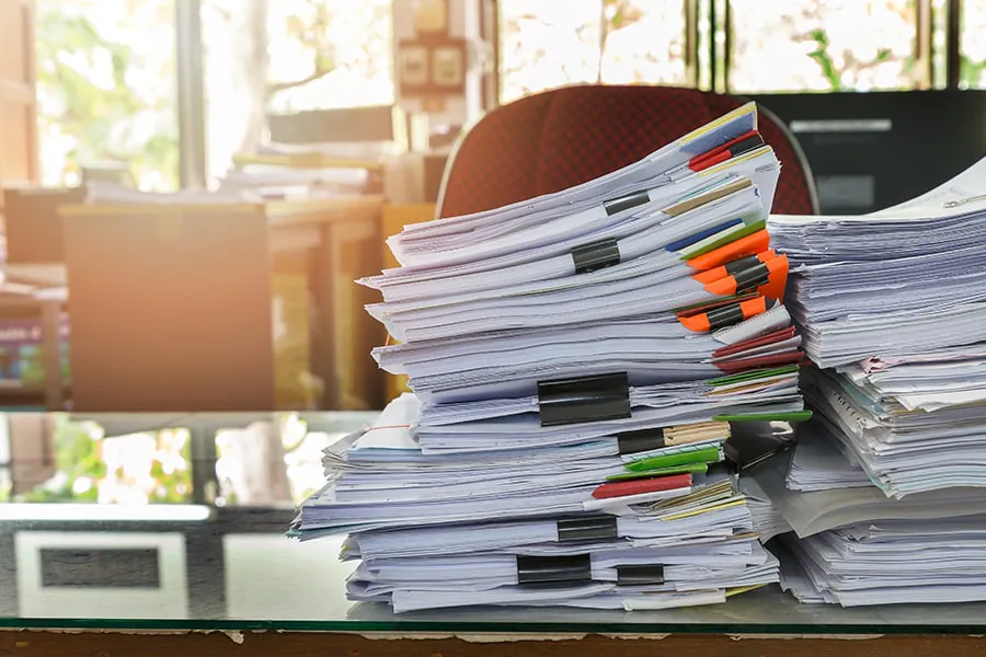 Tall stacks of business documents on an office desk